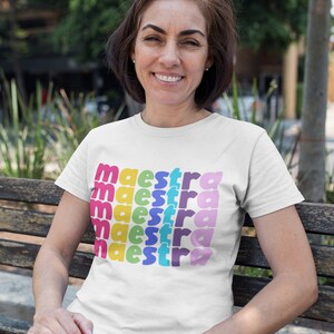May include: A white t-shirt with the word "maestra" repeated in rainbow colours.