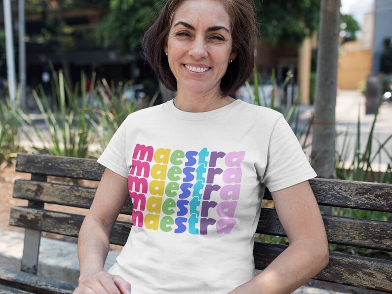 May include: A white t-shirt with the word "maestra" repeated in rainbow colours.