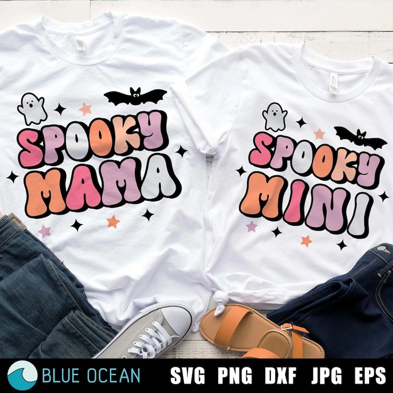 May include: Two white t-shirts with a Halloween theme. The larger shirt says "Spooky Mama" in pink, orange, and white letters with a ghost and bat graphic. The smaller shirt says "Spooky Mini" in the same colors with a ghost and bat graphic.