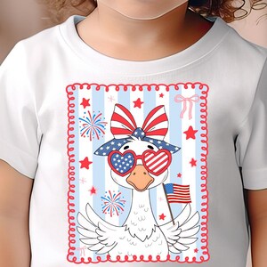 May include: White t-shirt with a cartoon goose wearing red, white, and blue sunglasses and a bow. The goose is holding an American flag. The background is blue and white stripes with stars and fireworks.