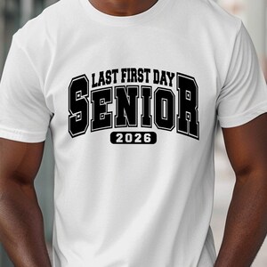 May include: White t-shirt featuring the text "LAST FIRST DAY SENIOR 2026" in a bold, black, block letter design. The shirt is made of a soft material and is suitable for casual wear. The design is centered on the front of the shirt.