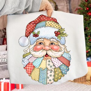 May include: A white pillow featuring a colorful illustration of Santa Claus. Santa's face is detailed with rosy cheeks, a white beard, and a red nose. His hat is red with white polka dots and a patchwork design.