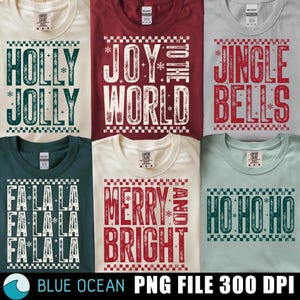 May include: A collection of Christmas-themed t-shirts in various colors, each featuring festive text designs. The shirts display phrases like "Holly Jolly," "Joy to the World," and "Jingle Bells" in bold, decorative fonts.