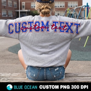 May include: A light grey long-sleeve sweatshirt featuring the words CUSTOM TEXT in a blue and red distressed varsity font across the back. The garment is worn with blue denim shorts. The text CUSTOM TEXT is printed in a bold, block-style lettering.