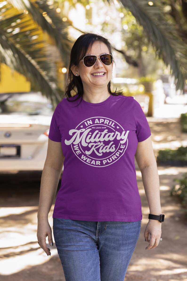 May include: A woman wearing a purple t-shirt with a white circle graphic that says "In April We Love Our Military Kids We Wear Purple".
