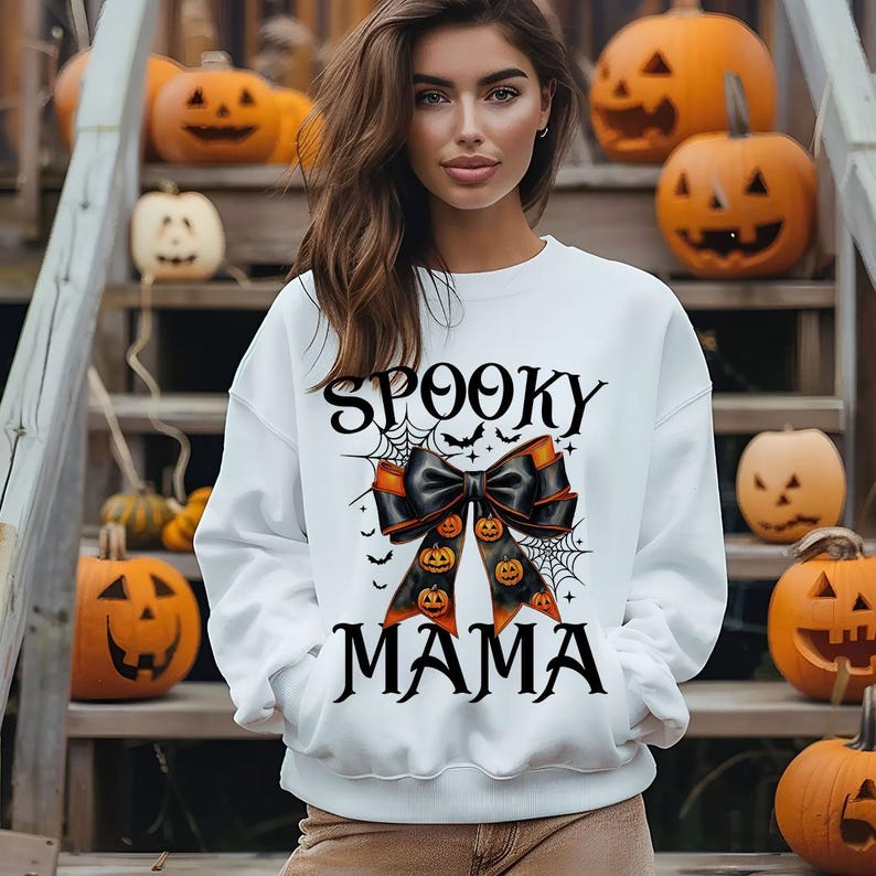 May include: White sweatshirt with a black and orange bow and the text "Spooky Mama" printed on the front.
