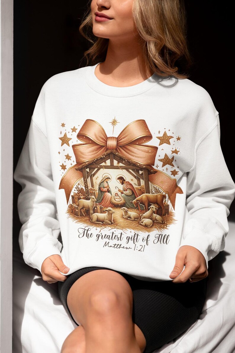 May include: White sweatshirt with a gold and brown illustration of the nativity scene. The illustration includes a bow, stars, and the text "The greatest gift of all Matthew 1:21".
