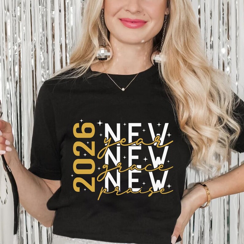 Peut inclure: T-shirt noir avec texte dor&eacute; "2026 New Year New Grace New Praise". Le t-shirt est de style col rond. L'image montre une femme portant le t-shirt.
