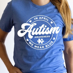 Puede incluir: Una camiseta azul con un gr&aacute;fico circular blanco que dice "En abril, conciencia del autismo, usamos azul" con una pieza de rompecabezas dentro del c&iacute;rculo.