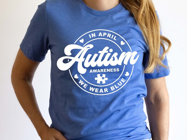 Puede incluir: Una camiseta azul con un gr&aacute;fico circular blanco que dice "En abril, conciencia del autismo, usamos azul" con una pieza de rompecabezas dentro del c&iacute;rculo.
