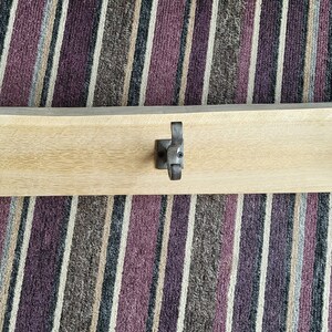 May include: A wooden coat rack with three metal hooks. The rack is light brown and the hooks are a dark silver colour.