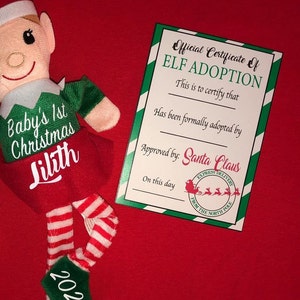 May include: A green and red elf doll with a certificate that reads "Official Certificate of Elf Adoption". The certificate states that "This is to certify that [blank] has been formally adopted by [blank] Approved by: Santa Claus. On this day [blank]" The elf doll has a name tag that reads "Baby's 1st Christmas Lilith 2020".