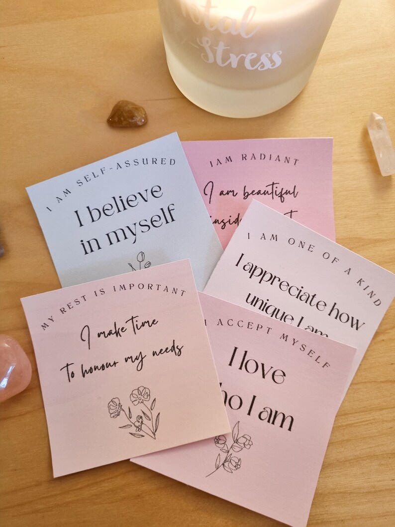 May include: Five pink and blue affirmation cards with positive messages about self-love, self-acceptance, and self-care. The cards feature simple floral illustrations and the text "I am self-assured, I believe in myself", "My rest is important, I make time to honour my needs", "I am radiant, I am beautiful inside and out", "I am one of a kind, I appreciate how unique I am", and "I accept myself, I love who I am".
