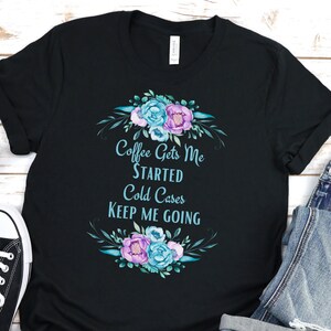 May include: Black t-shirt with a floral design and the text "Coffee Gets Me Started Cold Cases Keep Me Going".