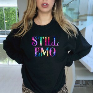 K&ouml;nnte beinhalten: Schwarzes Sweatshirt mit einem regenbogenfarbenen "STILL EMO"-Motiv.