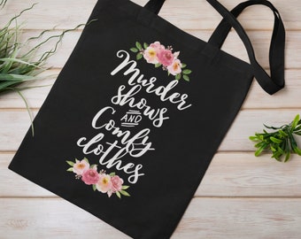 May include: Black tote bag with white text that reads "Murder shows and comfy clothes" with pink floral accents.