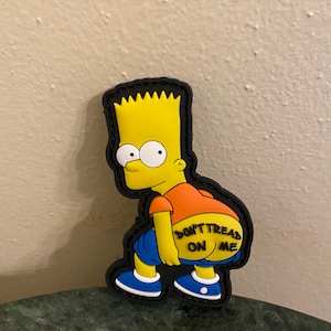 Puede incluir: Personaje de dibujos animados amarillo con el pelo de punta, vistiendo jeans azules y una camisa naranja, con el texto "Don't Tread On Me" en la espalda. El personaje está de pie sobre un fondo negro.