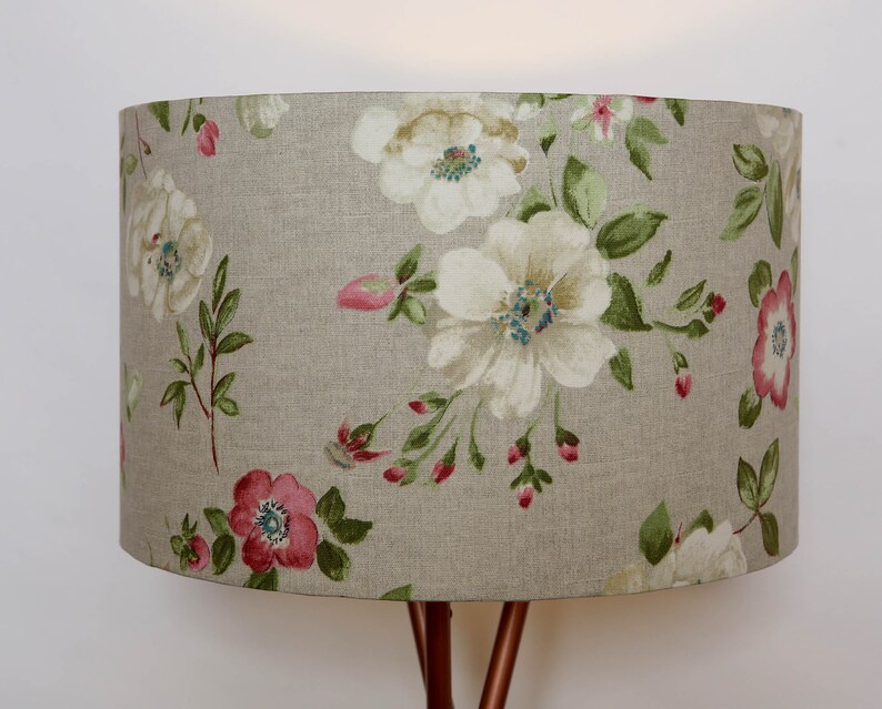 May include: A beige lampshade with a floral pattern featuring white and pink flowers and green leaves.
