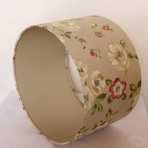May include: A beige lampshade with a floral pattern featuring white flowers, green leaves, and pink accents.