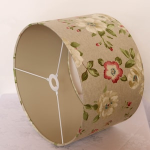 May include: A beige lampshade with a floral pattern featuring white, pink, and green flowers. The lampshade has a white fabric lining.