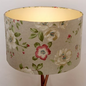 May include: A beige lampshade with a floral pattern featuring white, pink, and green flowers. The lampshade is made of fabric and has a white lining.