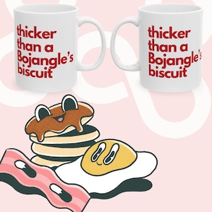 May include: White ceramic mug with red text that reads "thicker than a Bojangles' biscuit". The mug is next to a cartoon illustration of a stack of pancakes with syrup, a fried egg, and a strip of bacon.