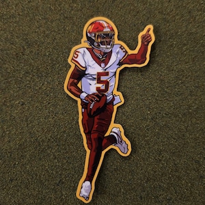 May include: A sticker depicting a football player in a red and white uniform, number 5, holding a football and pointing. The player wears a red helmet and is outlined in yellow.