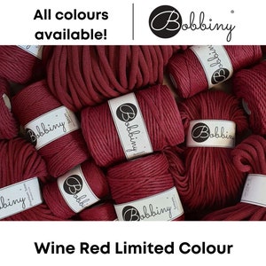 Puede incluir: Primer plano de varios carretes de cuerda de algodón roja gruesa. Cada carrete tiene una etiqueta blanca con la palabra "Bobbiny" impresa en ella. El texto "Wine Red Limited Colour" está impreso debajo de la imagen.