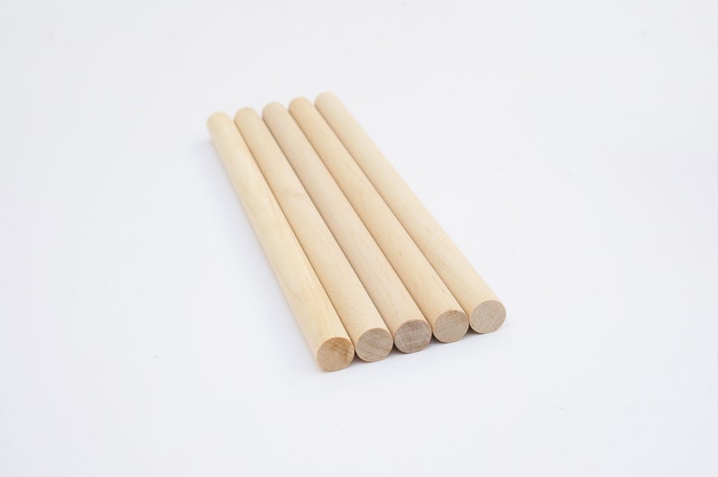 Puede incluir: Cinco clavijas de madera, todas del mismo tama&ntilde;o, est&aacute;n dispuestas en una fila sobre una superficie blanca. Las clavijas son de color marr&oacute;n claro y tienen un acabado liso y redondeado.