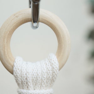 May include: A close-up of a wooden ring with a white cotton rope attached to it. The ring is hanging from a silver hook.