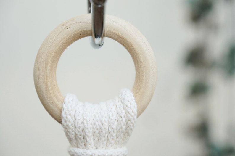 May include: A close-up of a wooden ring with a white cotton rope attached to it. The ring is hanging from a silver hook.