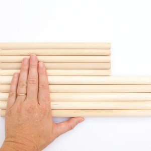 Puede incluir: Una pila de clavijas de madera, dispuestas en forma rectangular, con una mano apoyada en la parte superior de las clavijas.