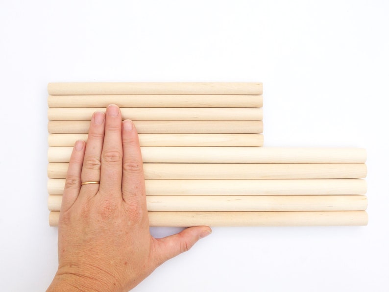 Puede incluir: Una pila de clavijas de madera, dispuestas en forma rectangular, con una mano apoyada en la parte superior de las clavijas.