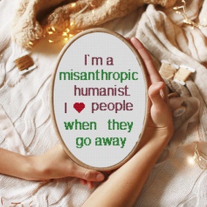 Pode incluir: Um aro de bordado branco com o texto "I'm a misanthropic humanist I ♥ people when they go away" em letras verdes e castanho-avermelhadas com um coração vermelho.