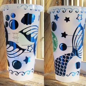 May include: Four white reusable cups with a mermaid tail design. The cups have a blue and black mermaid tail design with stars, bubbles, and seashells. The cups are decorated with a blue and black iridescent finish.