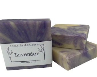 May include: Three rectangular bars of handmade soap with a marbled purple and cream swirl pattern. The front bar features a white paper label with the text Lucid Lather Soaps, Lavender, and Handmade soap enclosed in a simple line-drawn frame.