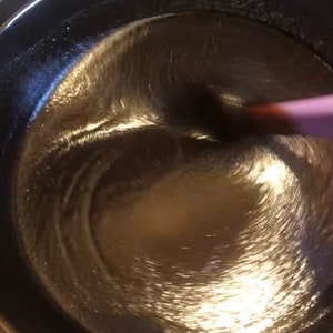 May include: A close-up of a dark brown liquid being stirred in a silver pot with a pink spatula.