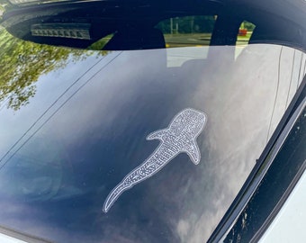 May include: A white car with a black whale shark sticker on the rear window.