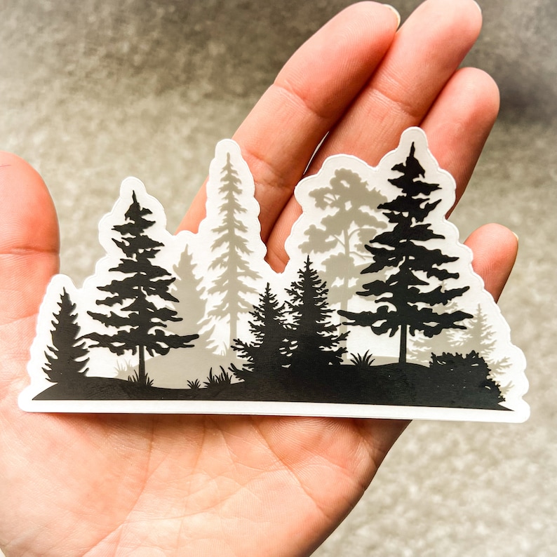 May include: A black and white sticker featuring a silhouette of a forest with multiple trees. The sticker is on a hand.