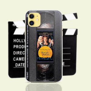 May include: A black and silver phone case with a Hocus Pocus VHS tape design. The case has a black background with a silver cassette tape design and the Hocus Pocus movie title and logo. The case has a black and silver camera lens cutout and a black and silver volume button cutout.