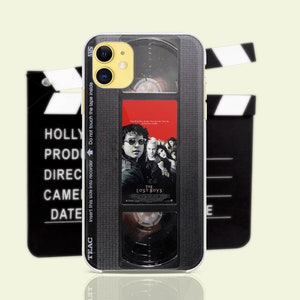 May include: A black and white iPhone case with a vintage VHS tape design. The case features a movie poster for "The Lost Boys" with the text "Insert this side into recorder Do not touch the tape inside" on the side.