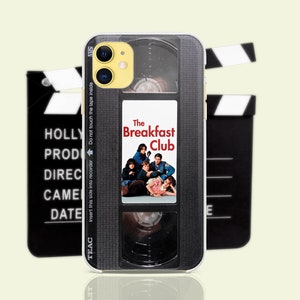 Può includere: Una custodia per iPhone nera e argento con un design a nastro VHS vintage. La custodia presenta il titolo del film "The Breakfast Club" e un gruppo di adolescenti del film.