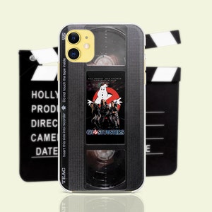 Peut inclure: Coque de téléphone noire avec un design de cassette VHS vintage représentant le logo et les personnages de Ghostbusters. La coque a un objectif d'appareil photo transparent et une bordure noire.