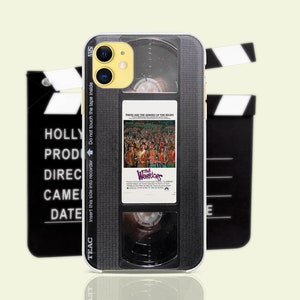 May include: A black and gray phone case with a VHS tape design. The case has a clear back and a black front with a silver label that says "The Warriors" and "These are the warriors of the night".