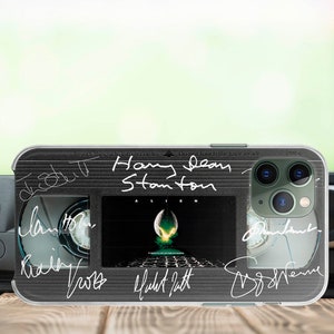 Op de afbeelding: Een zwarte en transparante telefoonhoes met een retro VHS-tape ontwerp. De hoes heeft een filmposter voor de film "Alien" met de tekst "Don't touch the tape-side" en verschillende handtekeningen, waaronder "Sigourney Weaver", "Harry Dean Stanton", "Ridley Scott", "H.R. Giger" en "James Cameron".