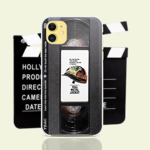 May include: A phone case featuring a design resembling a VHS tape with the movie title "Full Metal Jacket." The case has a black and white design with text that reads "Born to Kill." Two film clapperboards are in the background.