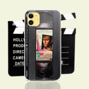 May include: A phone case featuring a retro VHS tape design with the movie "Cry-Baby" starring Johnny Depp. The case has a black and gray color scheme with text that reads "Insert this side into recorder" and "Do not touch the tape inside".