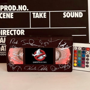 May include: A black VHS tape replica with a red light inside and a Ghostbusters logo. The tape is signed by the cast of the movie, including Bill Murray, Dan Aykroyd, Ernie Hudson, and Sigourney Weaver. The tape is accompanied by a remote control with color changing lights.