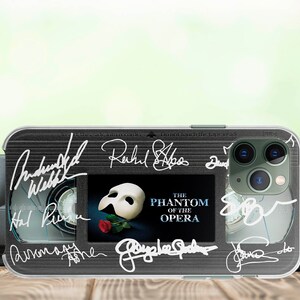 May include: A clear phone case with a black and white image of a VHS tape. The tape has the title "The Phantom of the Opera" and several signatures, including "Andrew Lloyd Webber" and "Sarah Brightman".