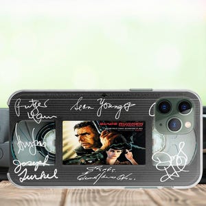 May include: A black and silver phone case with a clear plastic window displaying a movie poster for "Blade Runner". The case has a cassette tape design with signatures from the cast and crew, including Sean Young, Rutger Hauer, and Harrison Ford.